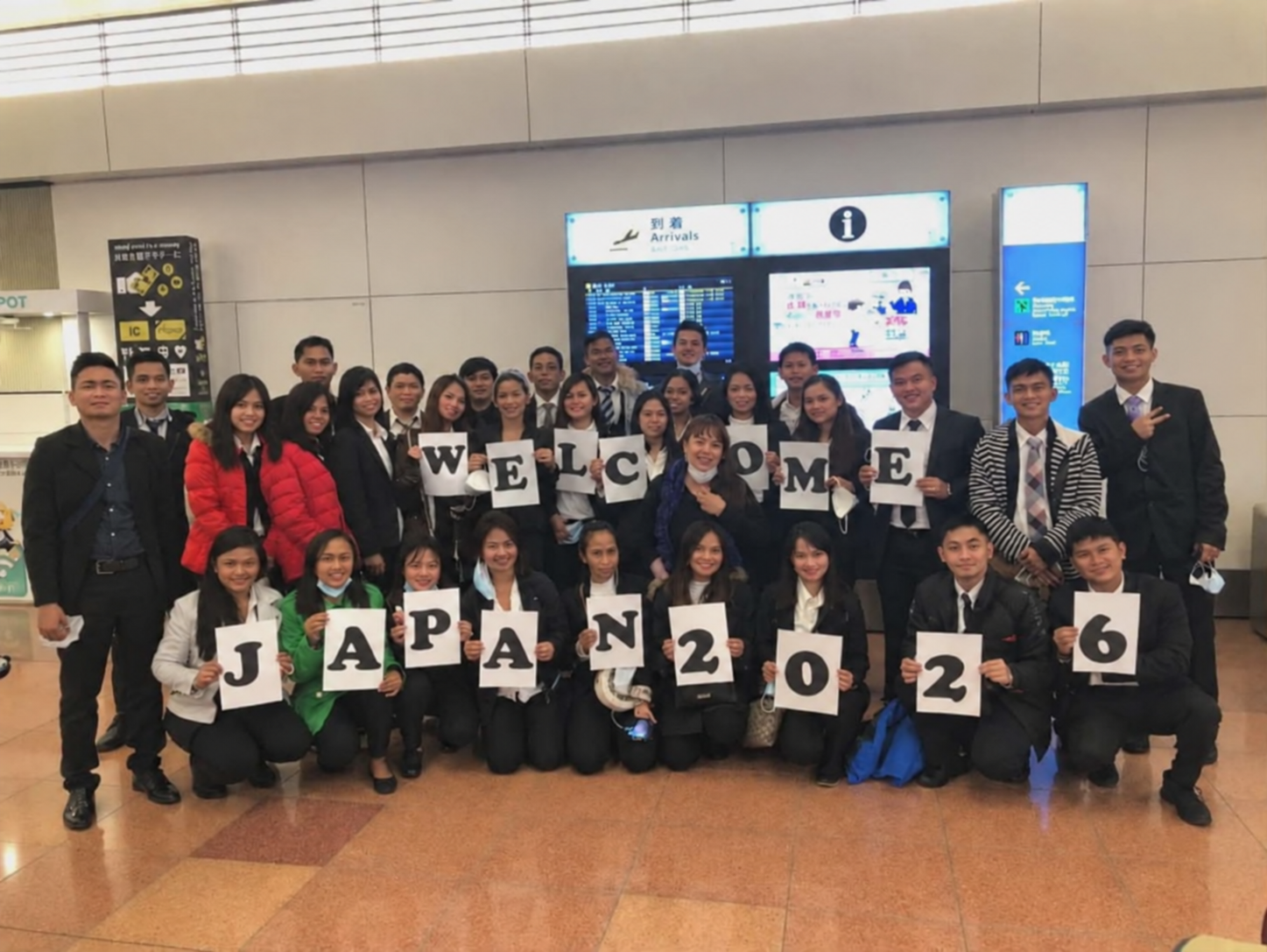 Grupo ng mga Pilipino sa airport sa Japan, hawak ang mga karatulang “Welcome Japan 2026.”