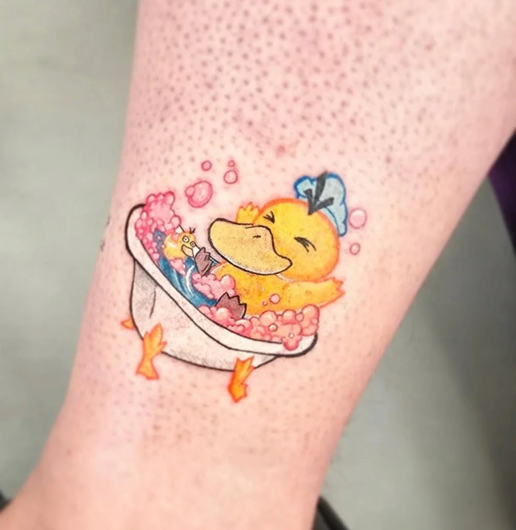 Tattoo of a cartoon duck in a bathtub filled with pink bubbles, with a blue bow on its head, smiling and winking.