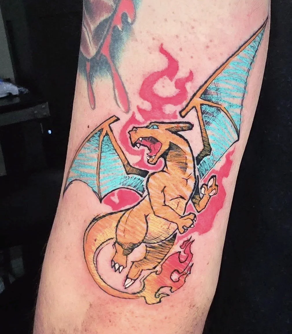 Tattoo of Charizard, a fiery orange dragon Pokémon with blue wings, breathing fire with pink flames behind it.