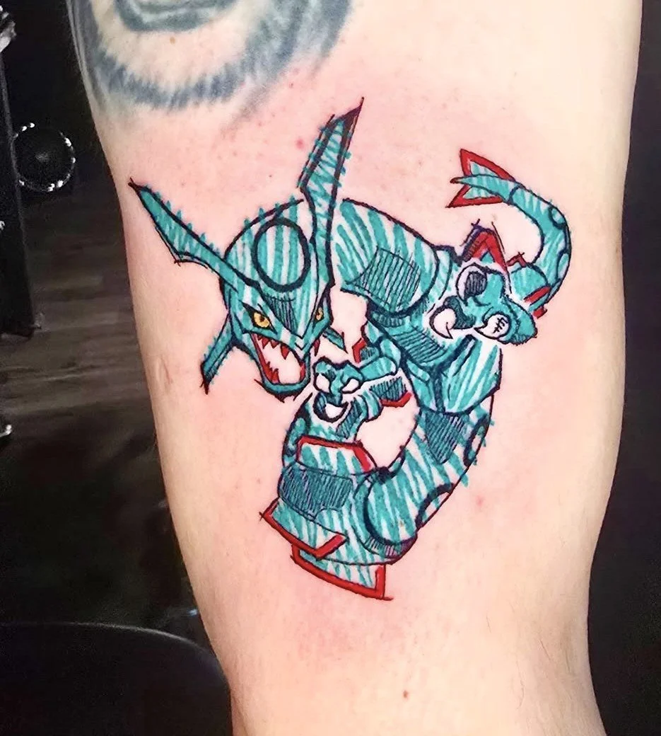 A colorful tattoo of the Pokémon Garchomp on a person's thigh, featuring blue, teal, red, and black ink in a sketch style.