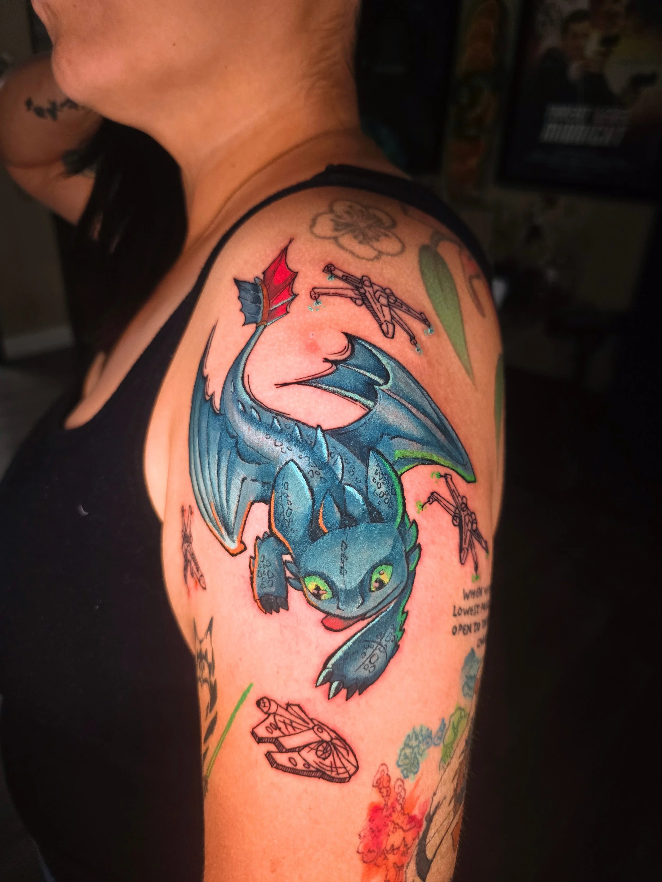 Tattoo of a blue dragon with red eyes and green accents on a person's upper arm, including smaller detailed tattoos nearby.