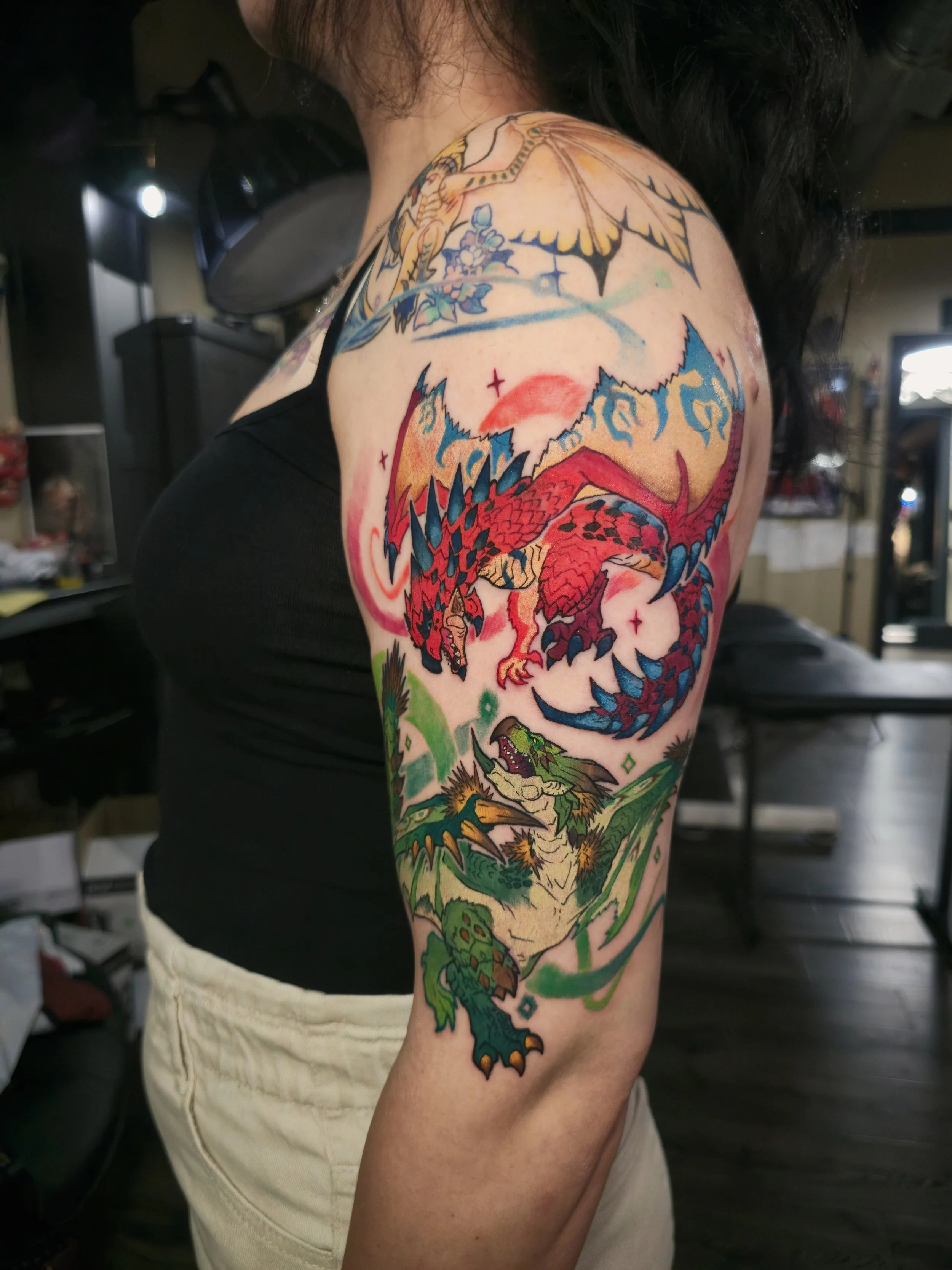 Colorful tattoo of a red and green dragon wrapping around the person's upper arm, with a mountain landscape and a sun or moon in the background.