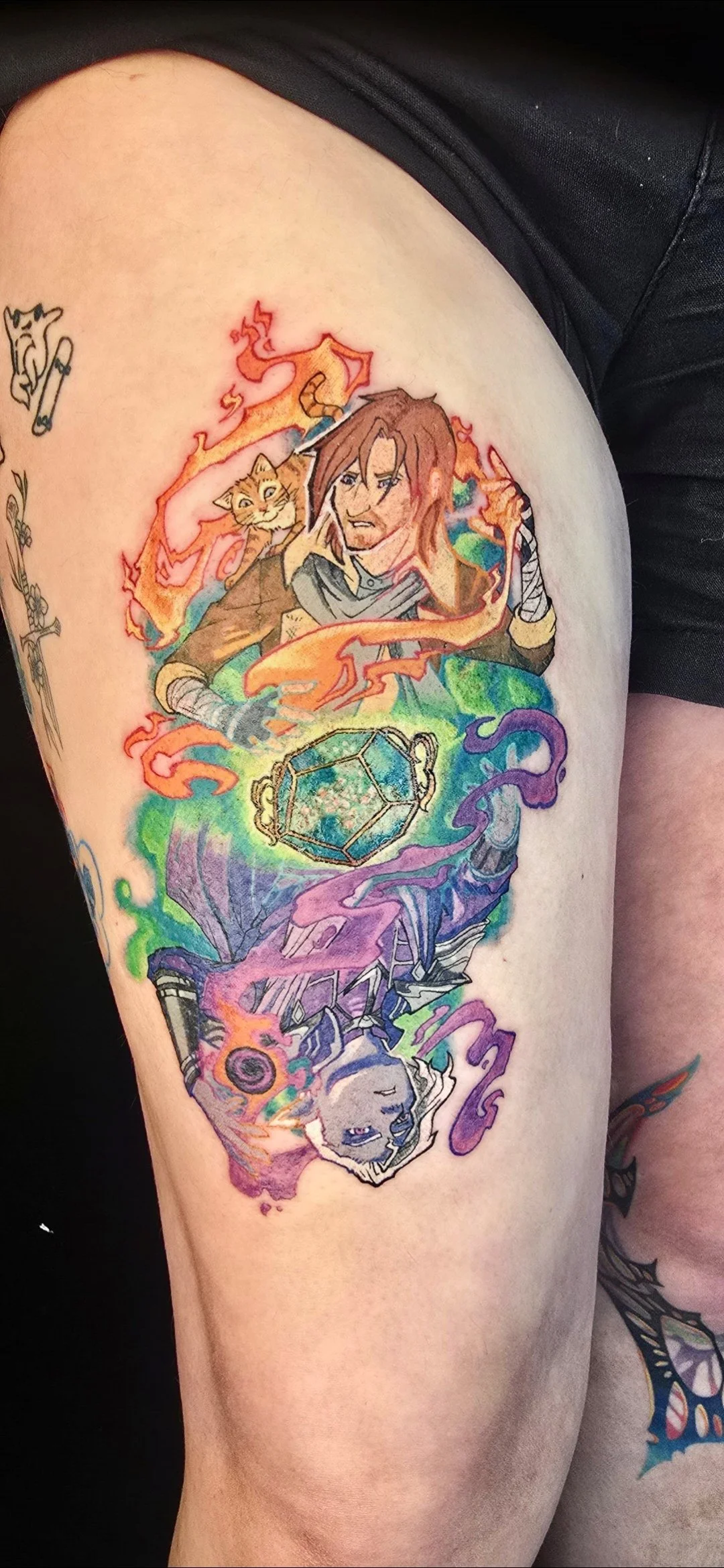 Colorful tattoo on person's thigh depicting a fantasy scene with a warrior, a cat with a sword, a glowing gemstone, a robotic figure, and vibrant swirls.