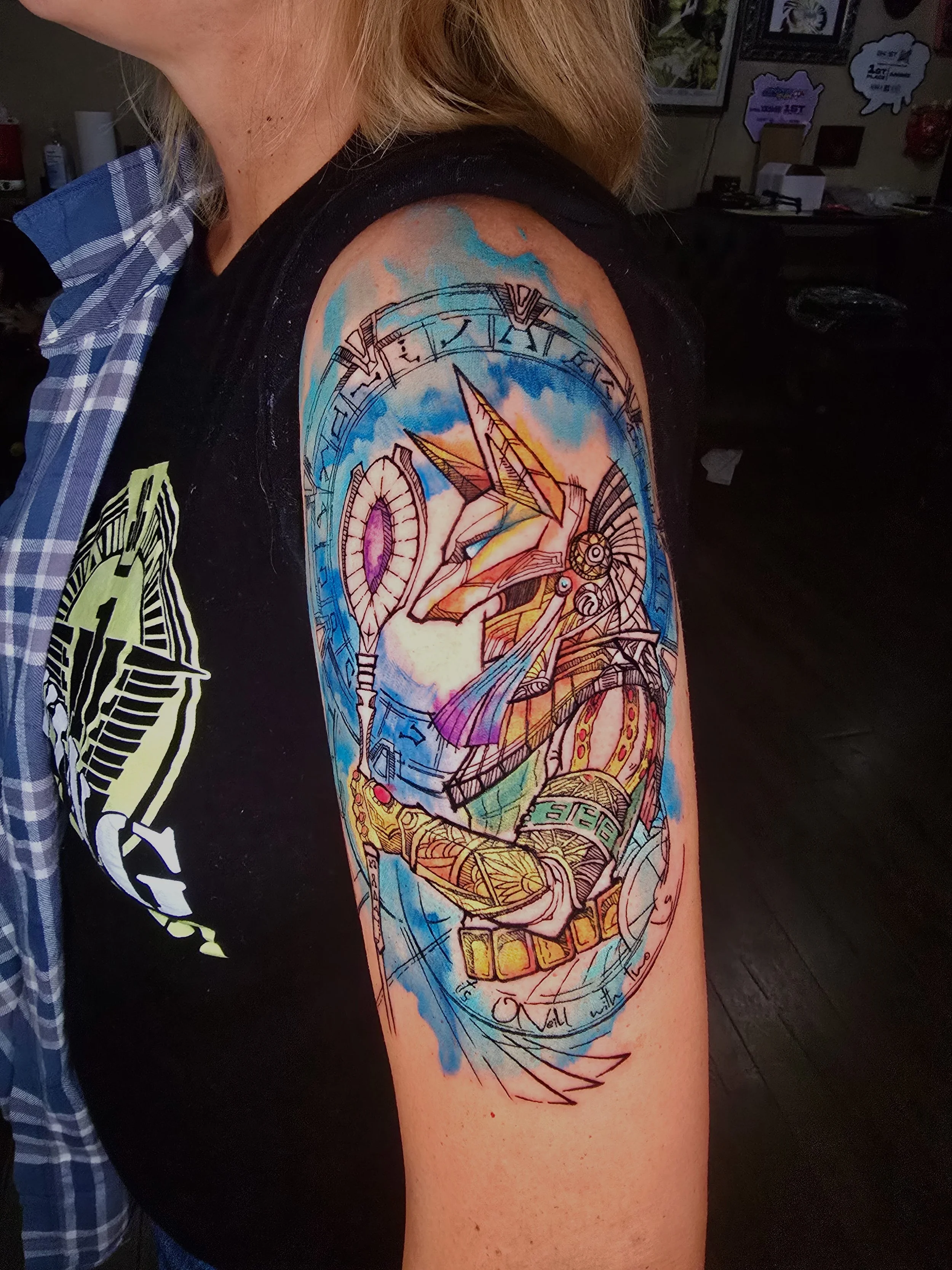 Colorful sleeve tattoo featuring a detailed science-fiction robotic hand, gears, lines, and features geometric shapes, with a background of blue and orange hues on a person's upper arm.