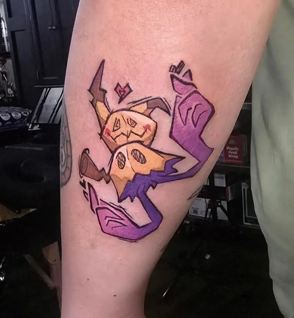 A colorful tattoo of a cartoonish pumpkin with a carved face, surrounded by purple, orange, and yellow abstract shapes on a person's arm.