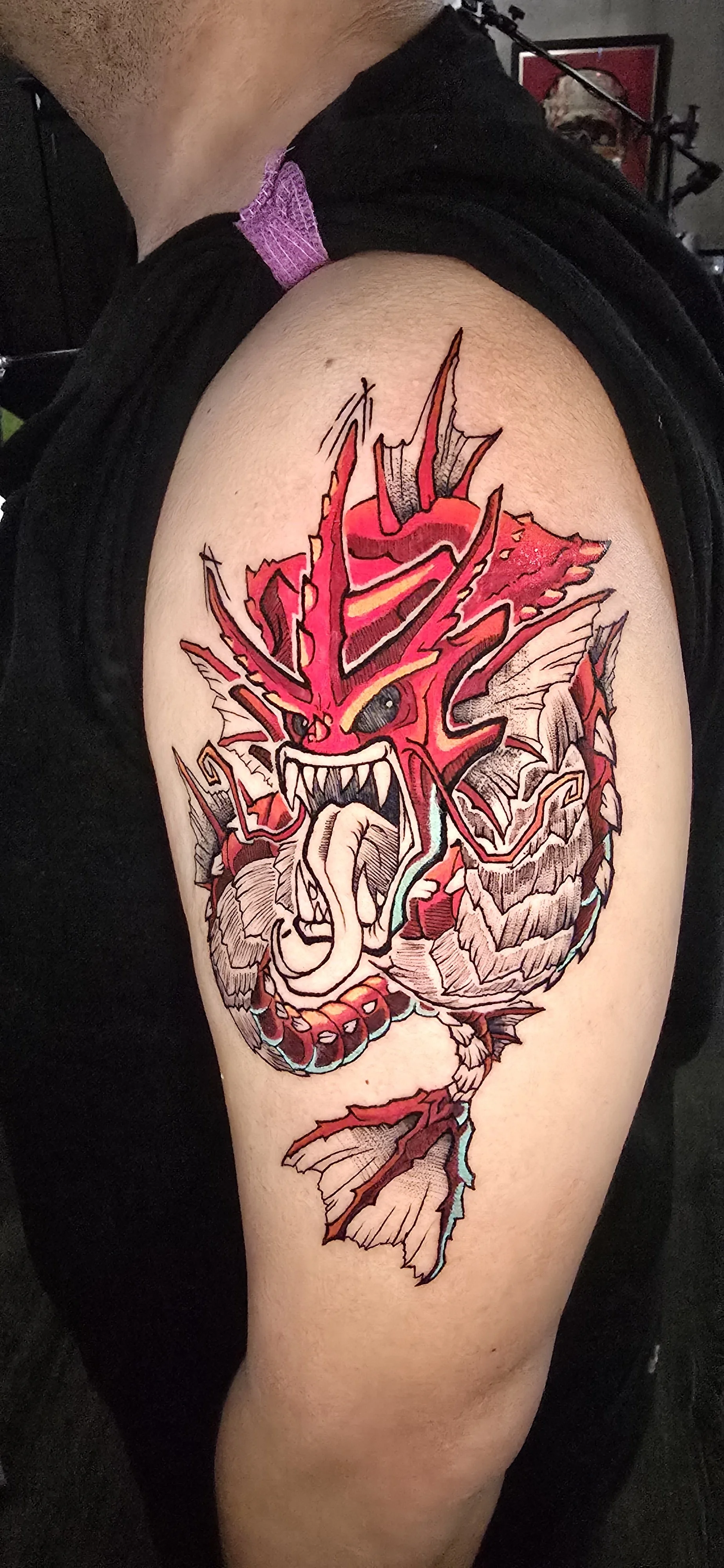 Colorful tattoo of an angry, fire-breathing dragon on person's upper arm.