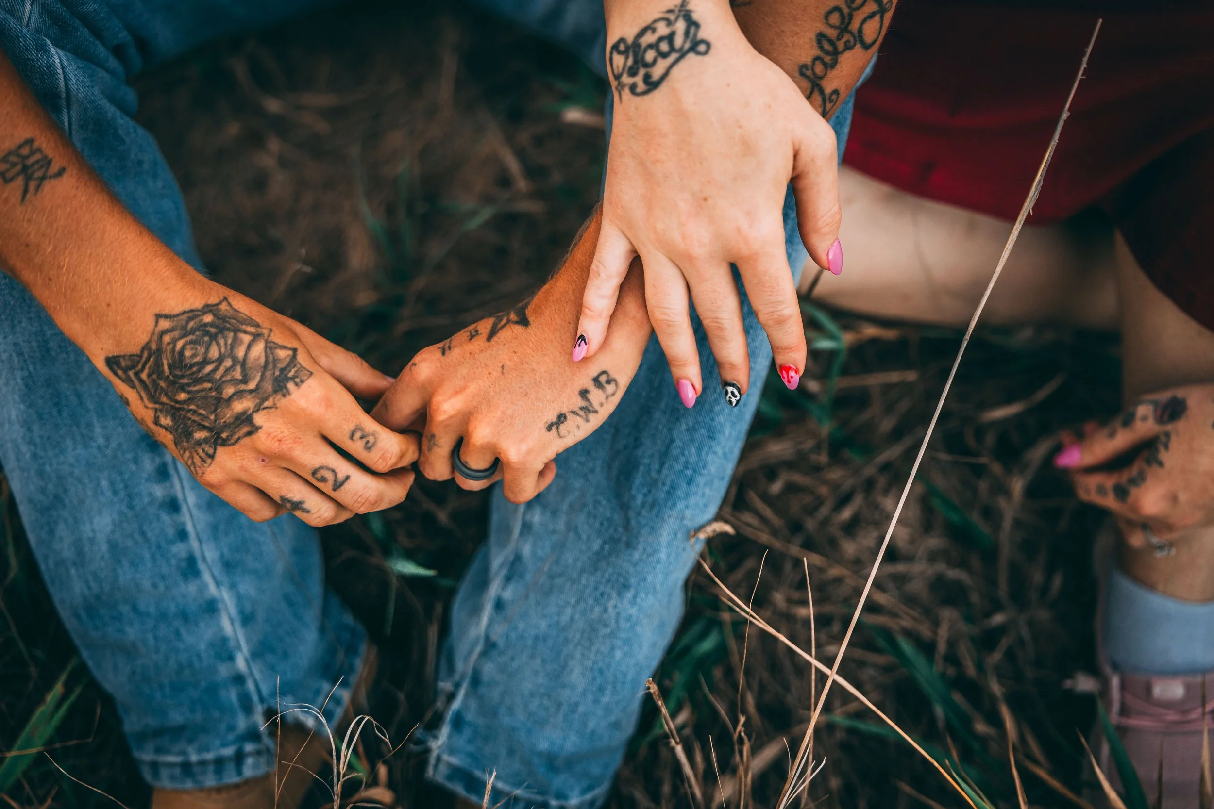 Close-up of tattooed people sitting outdoors with interlocked hands, colorful manicured nails, jeans, and a guitar string visible