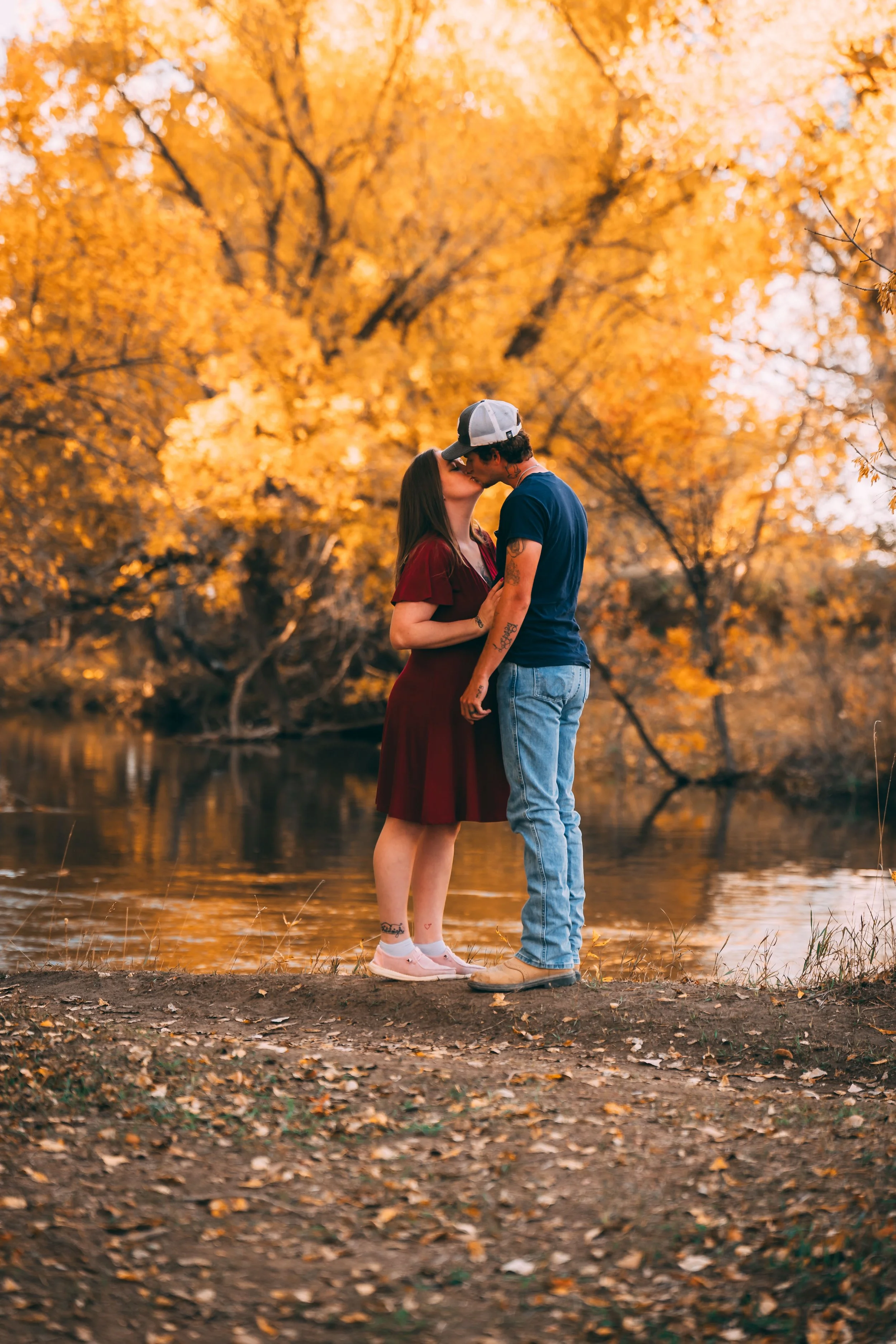 Couple kissing beside a lake surrounded by golden autumn trees