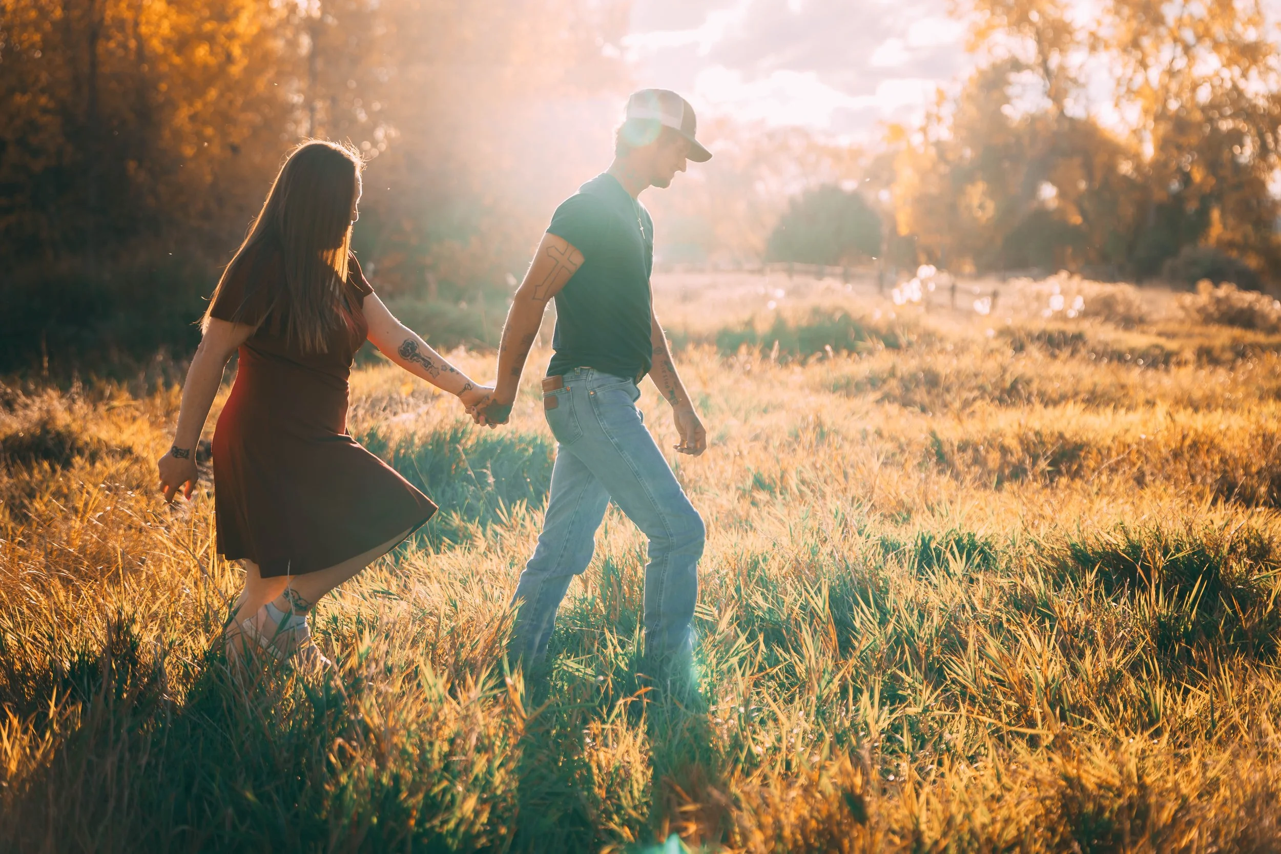 Couple holding hands while walking through a sunlit meadow at golden hour