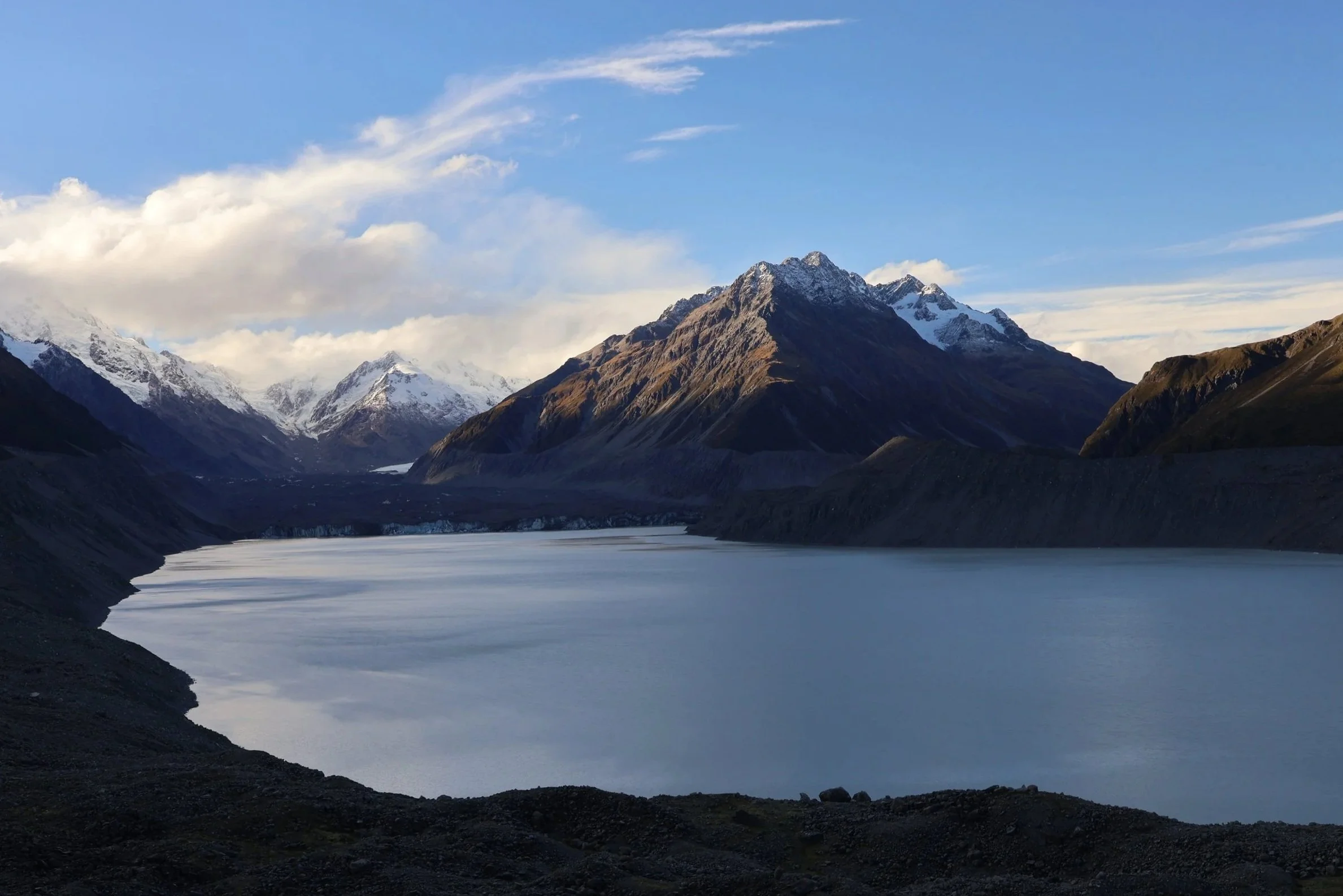 Photograph of Tasman Glacier Lake, New Zealand on a still sunny day with Tasnam Glacier and surrounding mountains.