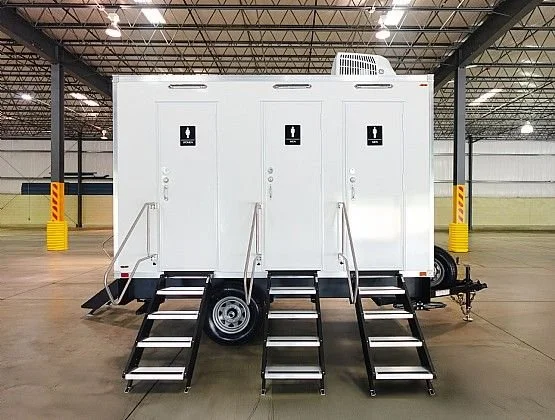 Mobile restroom trailer with three separate doors, accessibility ramps, located inside a large warehouse or parking structure.
