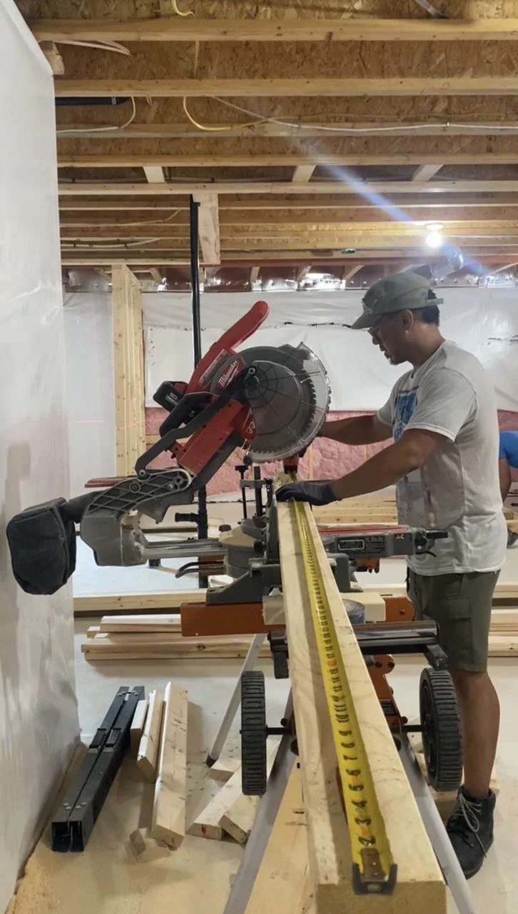 Contractor measuring lumber beside a Milwaukee miter saw at a home construction site