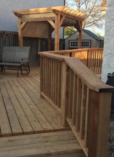 Wooden backyard deck with railings, pergola, outdoor seating, and a small shed.