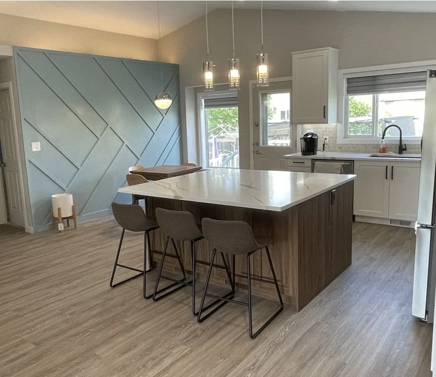 Modern kitchen with large marble island, four bar stools, white cabinets, pendant lights, and blue geometric accent wall
