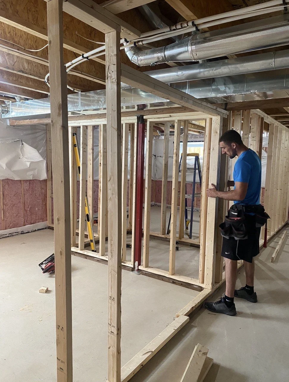 Contractor framing basement walls beneath exposed HVAC ductwork and insulation during home renovation.