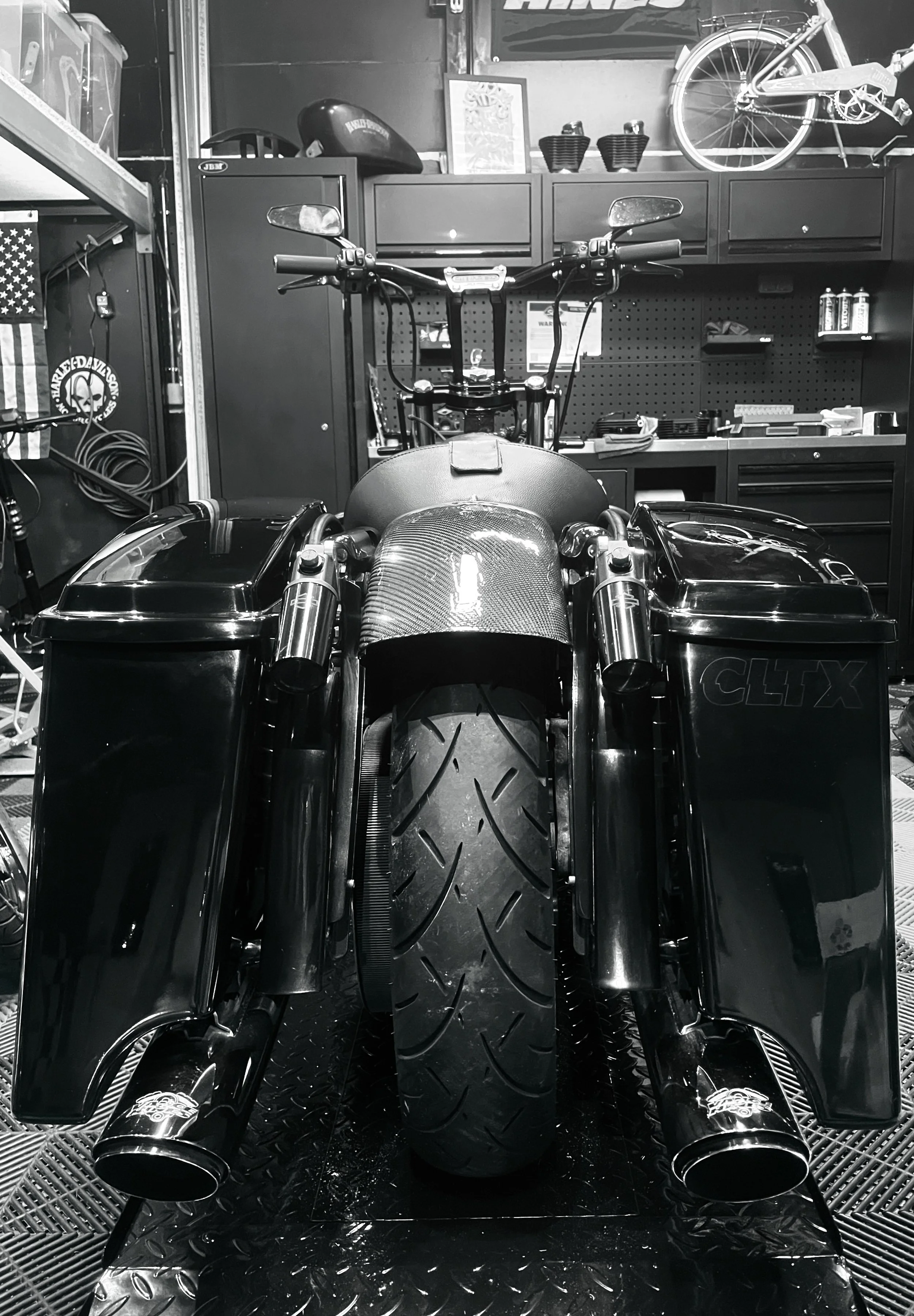 Vue frontale d'une moto sportive dans un garage, avec un pneu en avant, des garde-bousses, et des accessoires divers en arrière-plan.
