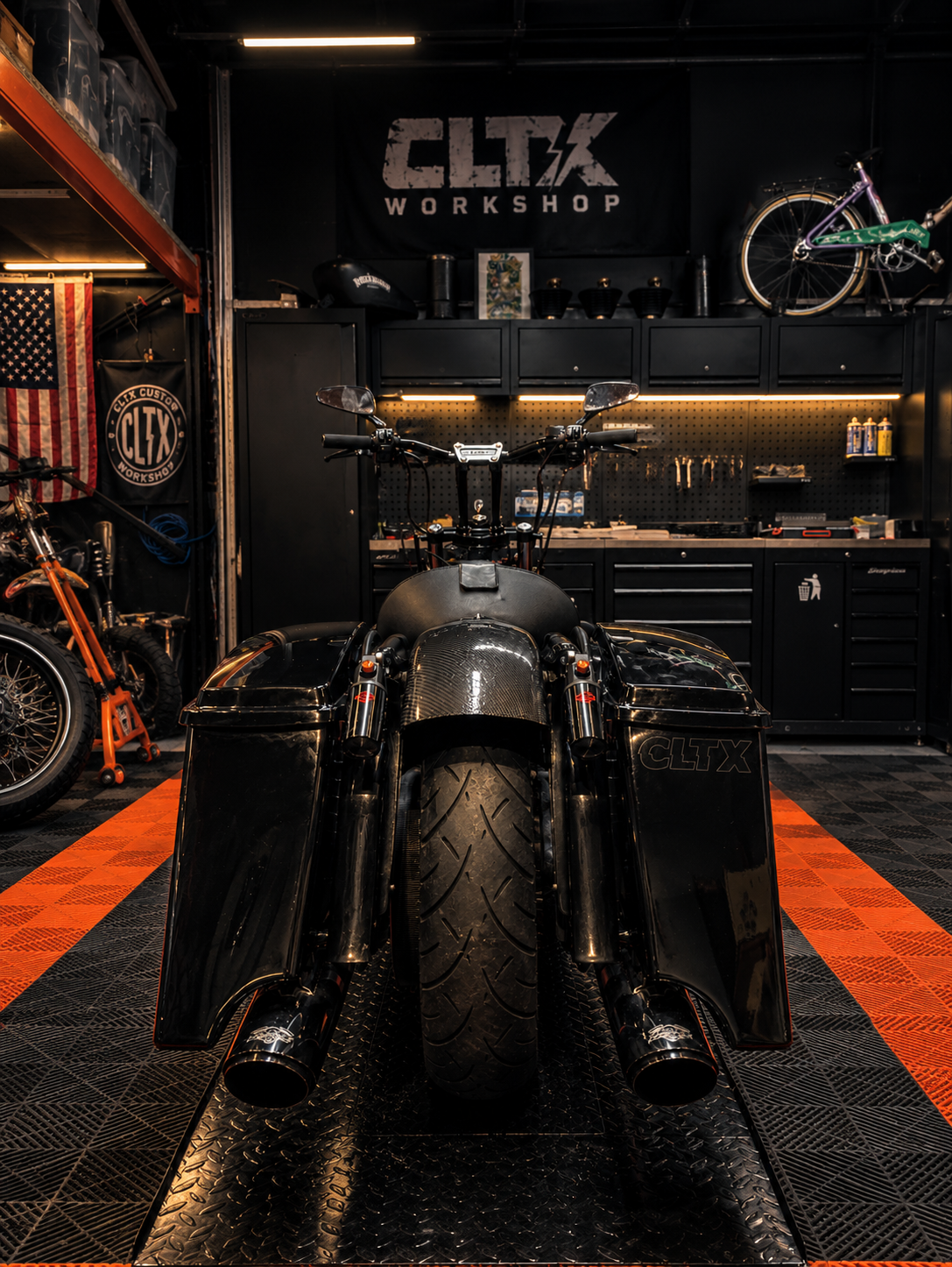 Une moto noire de course dans un atelier clef en main, avec des étagères, des outils et des vélos en arrière-plan.
