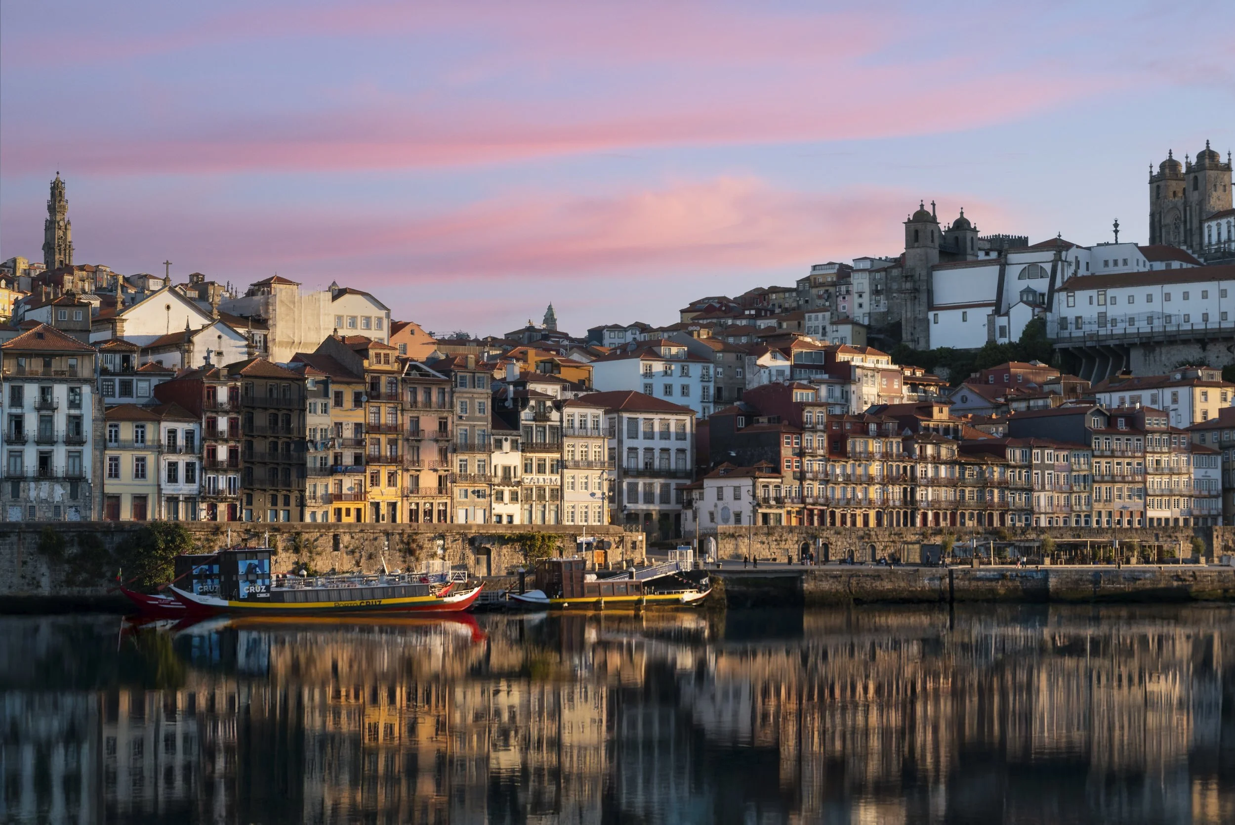 Panoramic view of Porto, Portugal, with colorful riverside buildings, historic churches, boats, and reflections on the Douro River at sunset
