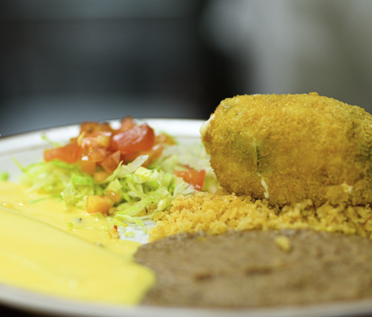 Plate with fried fish fillet, salad with shredded lettuce and chopped tomatoes, yellow rice, brown gravy, and yellow sauce.