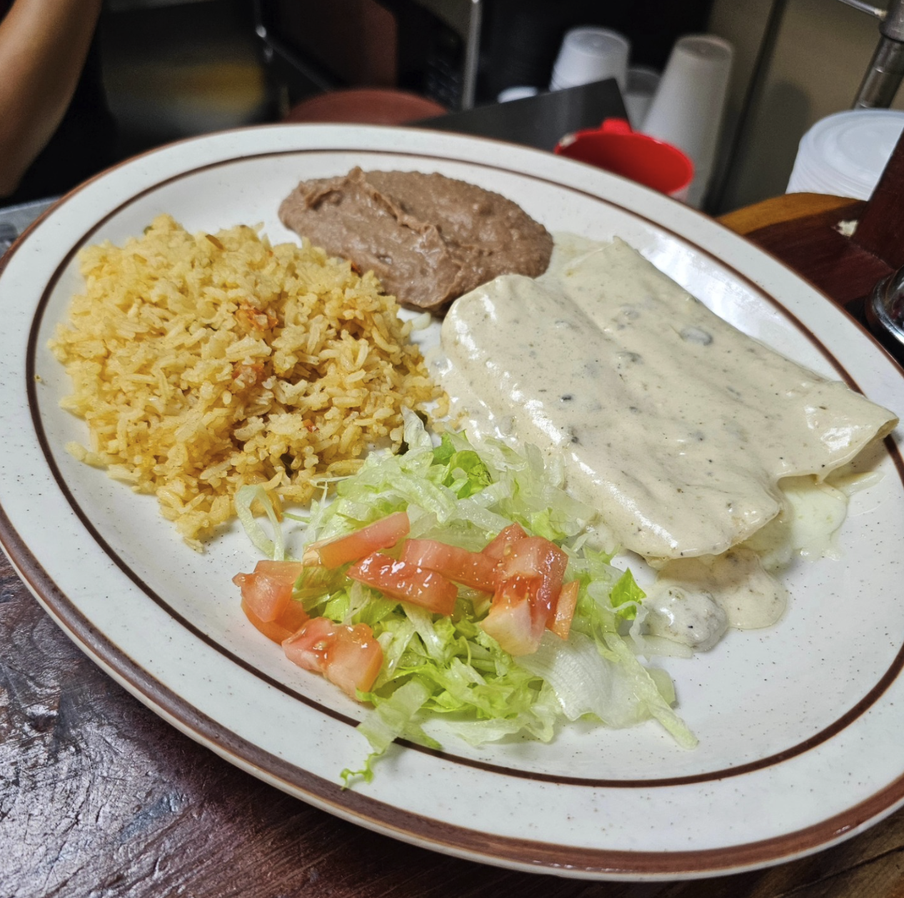 A plate of Mexican food with rice, shredded lettuce and tomato, chicken with white cream sauce, and sliced Mexican meat.