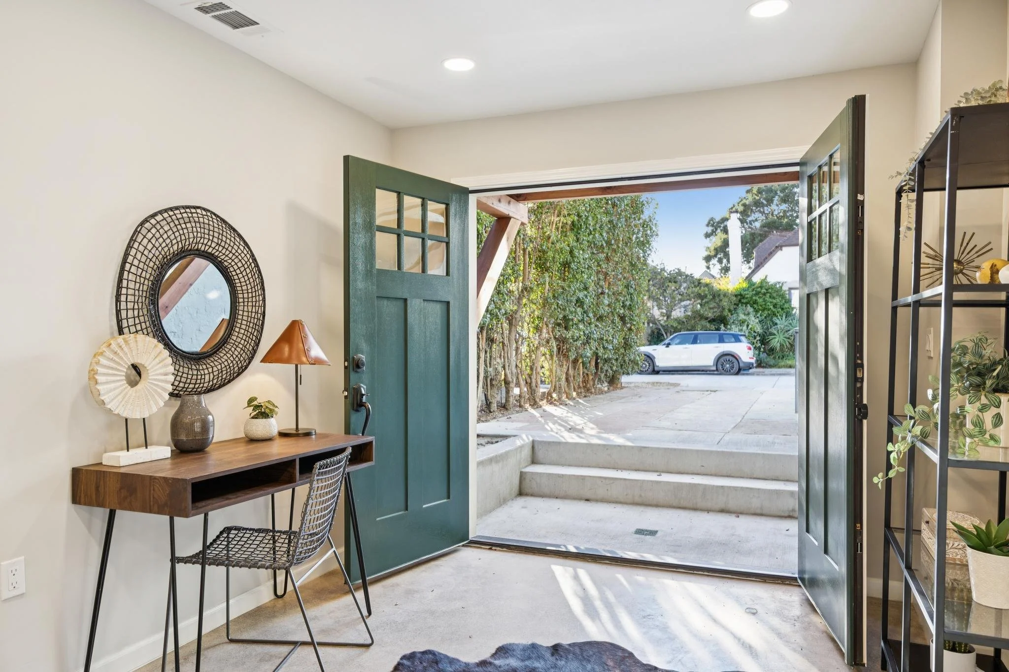Open front door view showing a sidewalk, trees, and a white car outside under a blue sky.