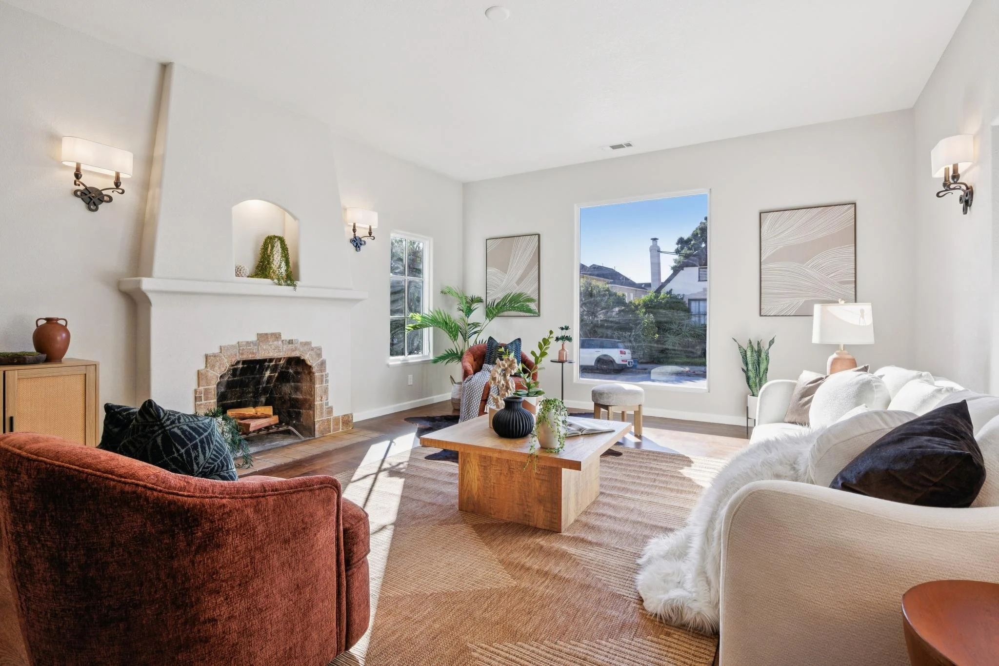 Bright living room with white walls, large windows, a fireplace, and various chairs and sofas, decorated with plants and artwork.