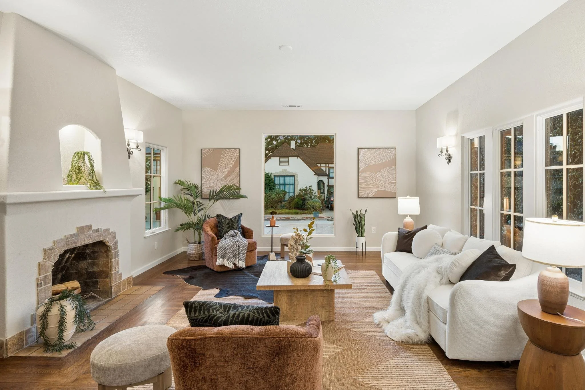A bright living room with white walls, large windows, a fireplace, and comfortable chairs and sofas decorated with pillows.
