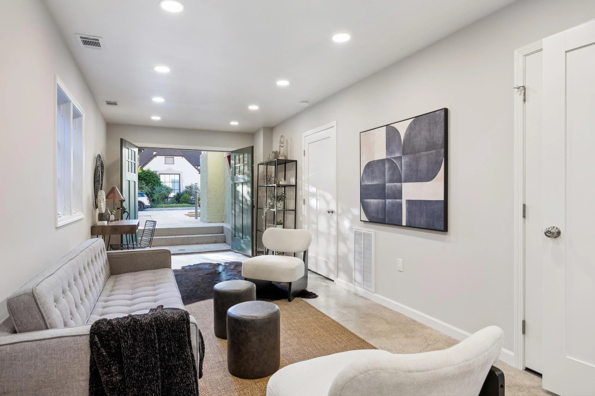 Living room with open front door, modern art wall piece, various chairs, lamps, and decorative items, with indoor-outdoor view.