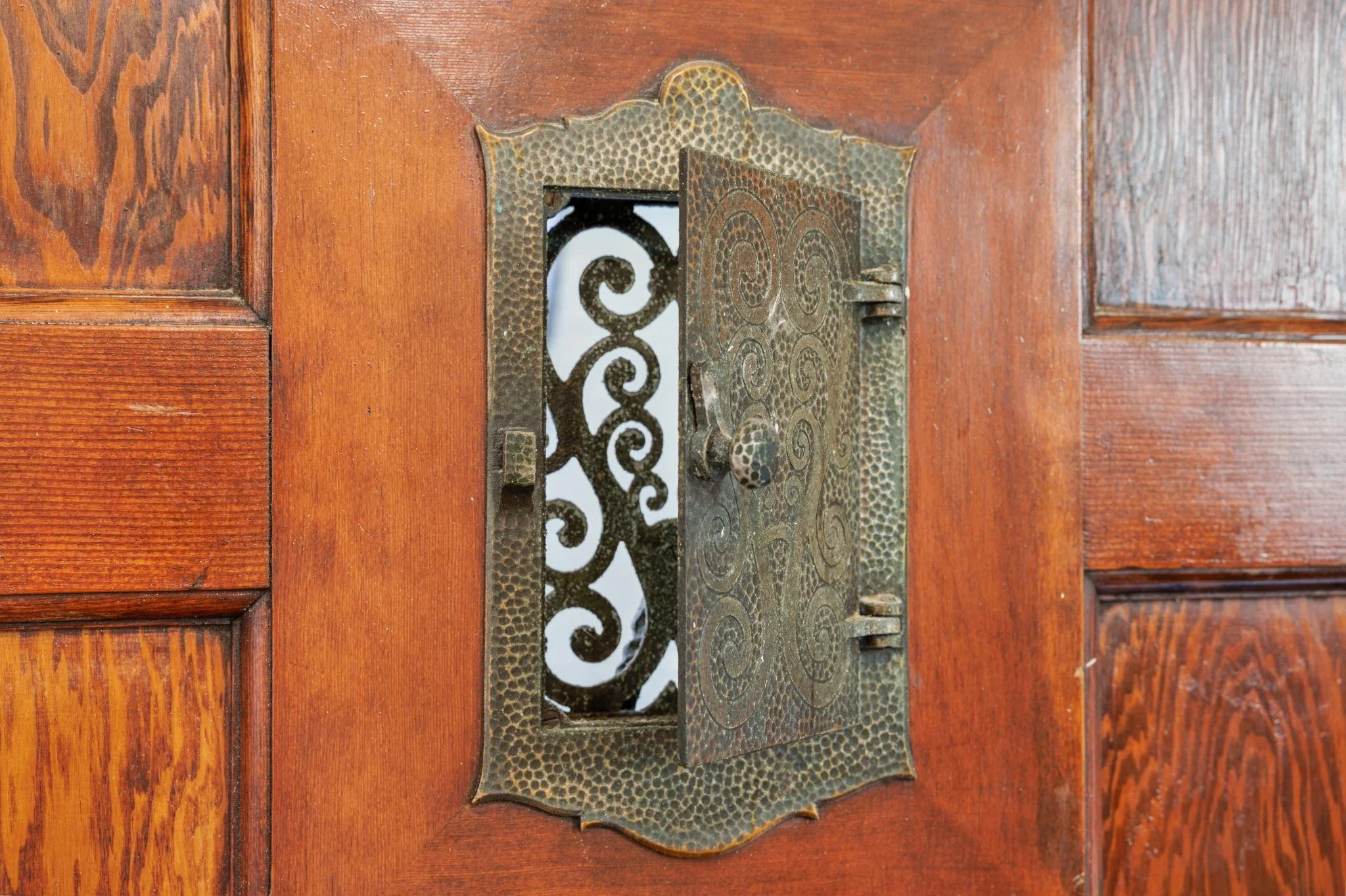 Close-up of a vintage brass door latch with intricate spiral and textured patterns, mounted on a wooden door.