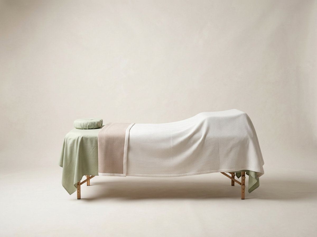 A massage table covered with soft, neutral-colored linens and towels in a minimalist, light-colored room.