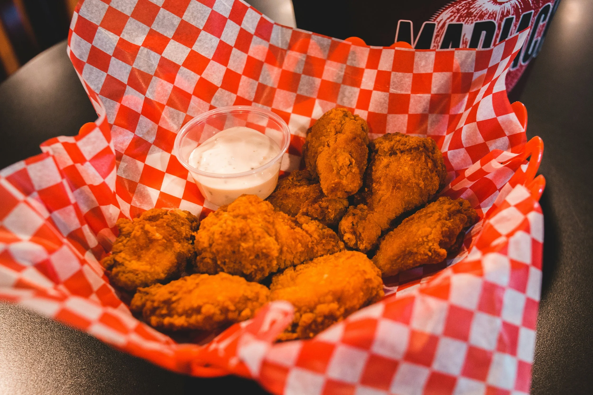 Fried chicken tenders in a red and white checkered basket with a small cup of ranch dipping sauce.