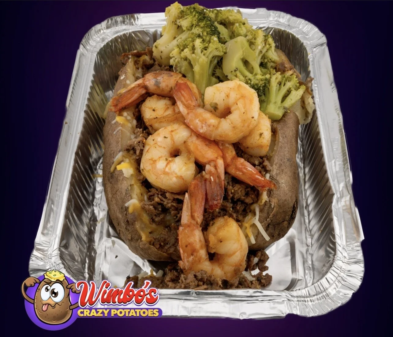 Baked potato topped with shrimp, beef, melted cheese, and broccoli, served in a takeout aluminum tray from Wimby's Crazy Potatoes.