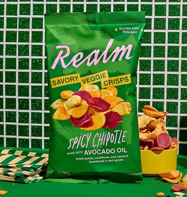A bag of Realm Chips, Spicy Chipotle Flavor, on a green tiled background.