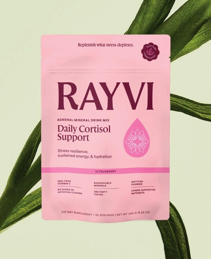 A pouch of Rayvi Daily Cortisol Supplement on a soothing green background with a macro image of a plant behind.