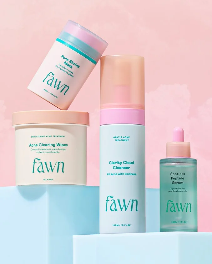 All four Fawn Teen Skincare products sit on light blue risers in front of a pink sky with subtle clouds.