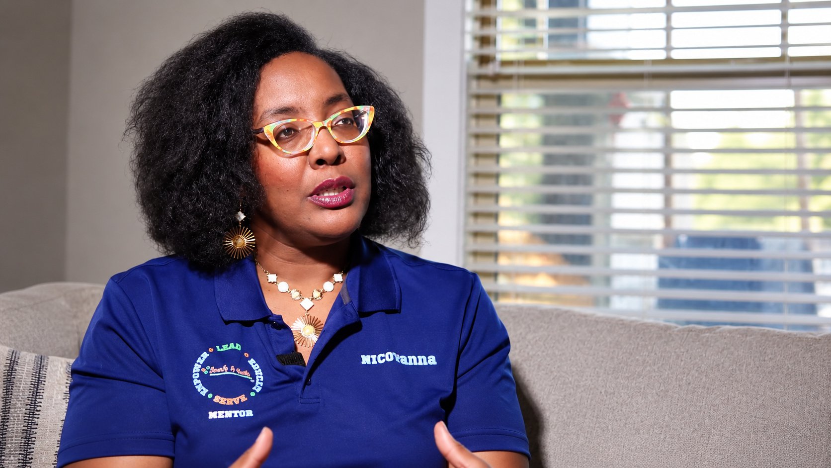 Interview production still featuring a woman wearing a blue polo shirt and colorful glasses, by Pugh Logic Productions.