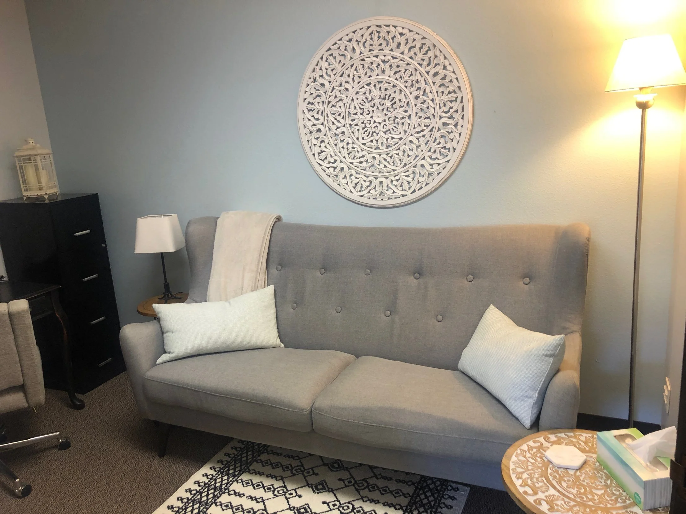 Calm counseling room at Safe Harbor Counseling Center with a gray sofa, soft lamps and a carved wall medallion