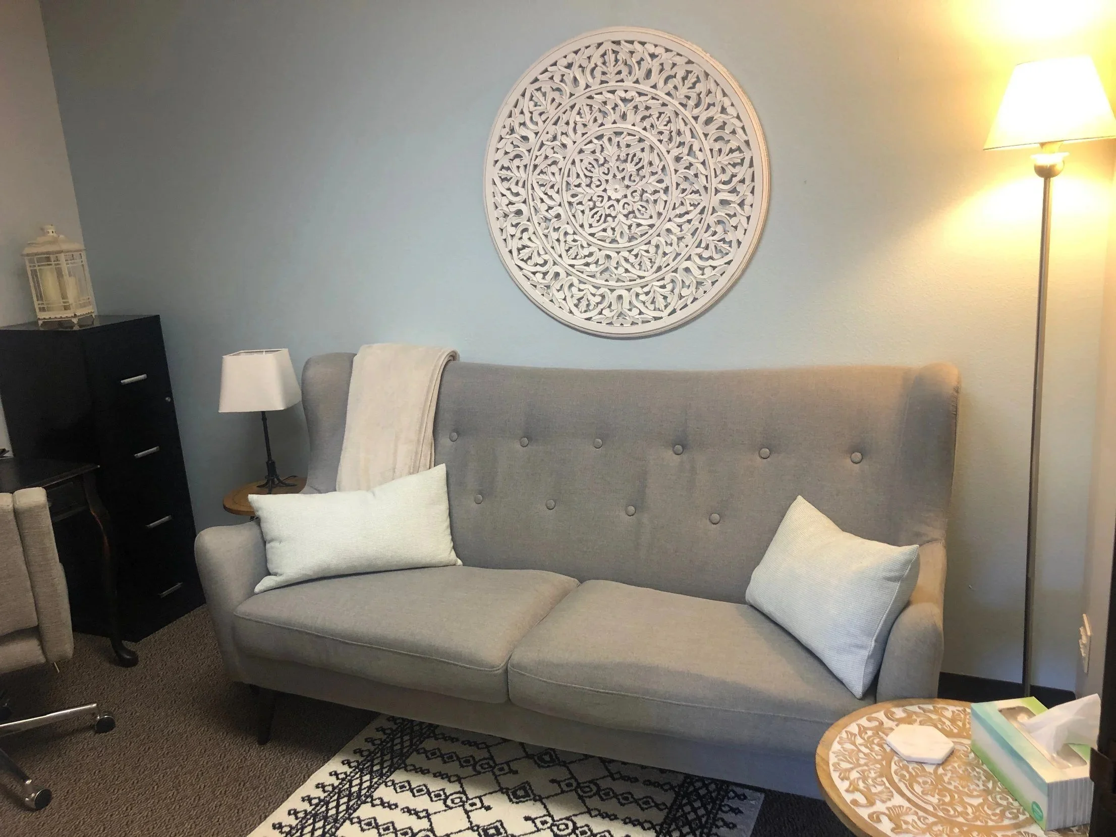 Calm counseling room at Safe Harbor Counseling Center with a gray sofa, soft lamps and a carved wall medallion