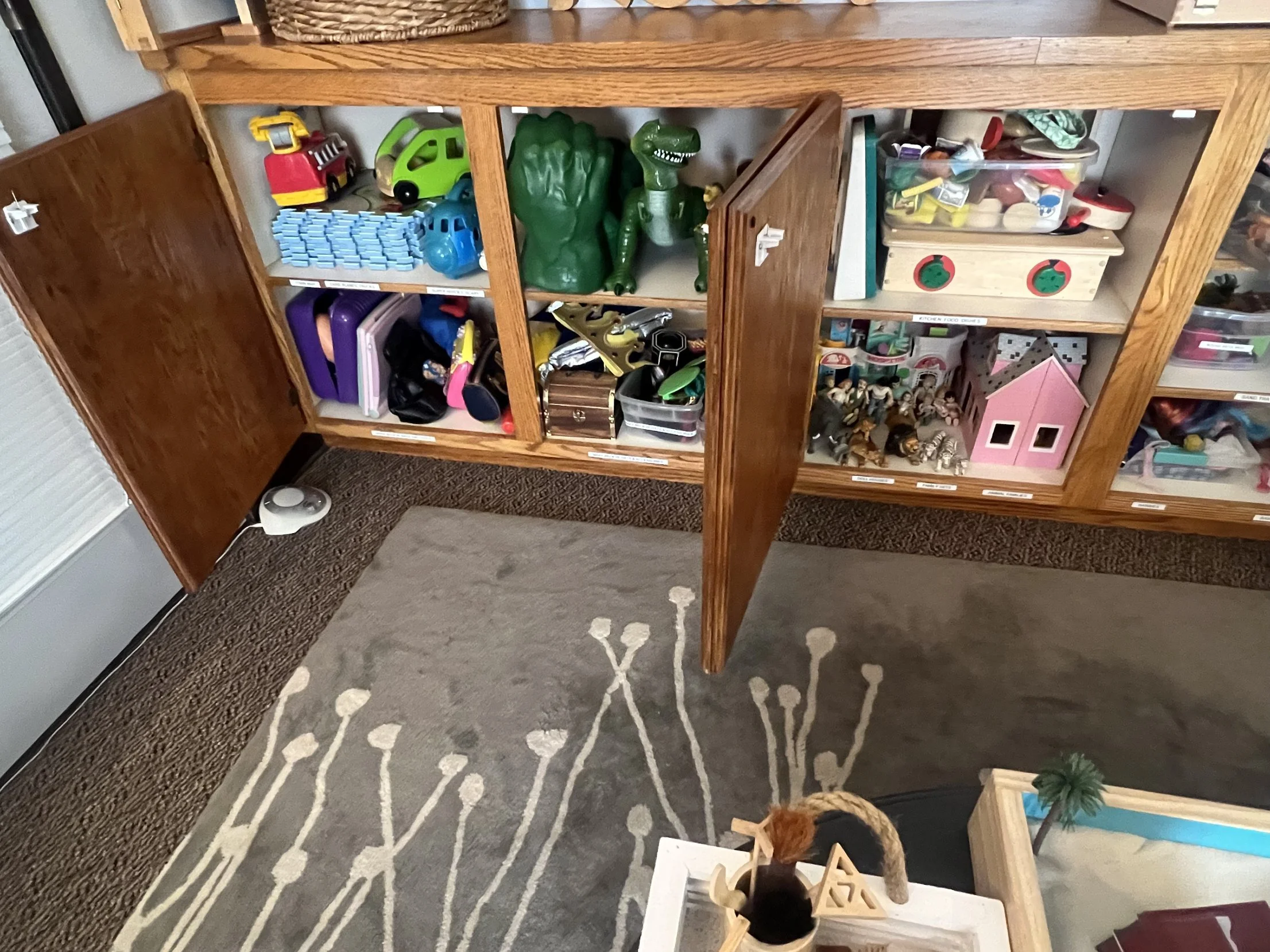 Labeled shelves of toys, dollhouses, animals and dress-up items in the play therapy room at Safe Harbor Counseling Center