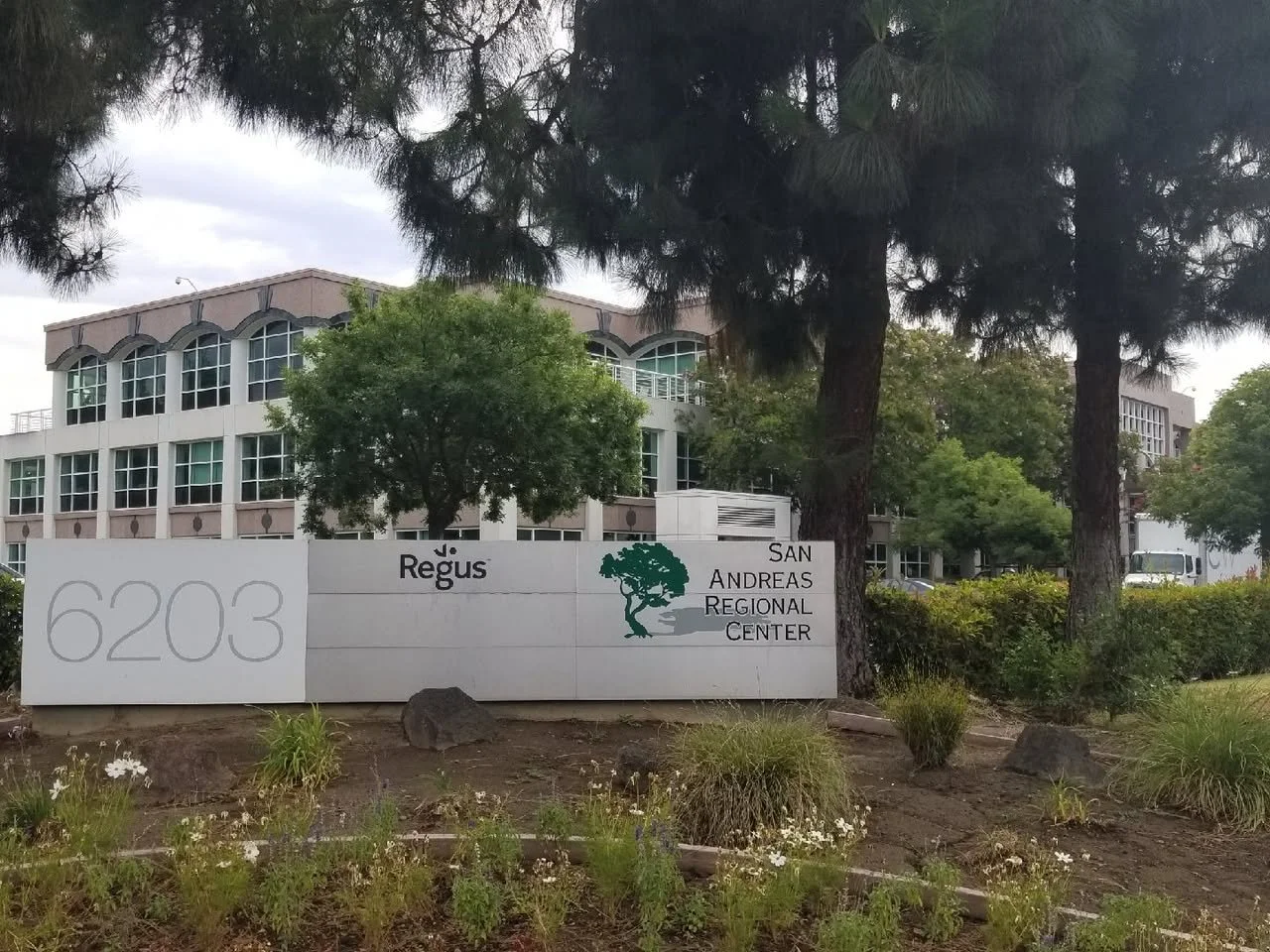 Sign indicating the address 6203 for the Regus San Andreas Regional Center, with a building and trees in the background.
