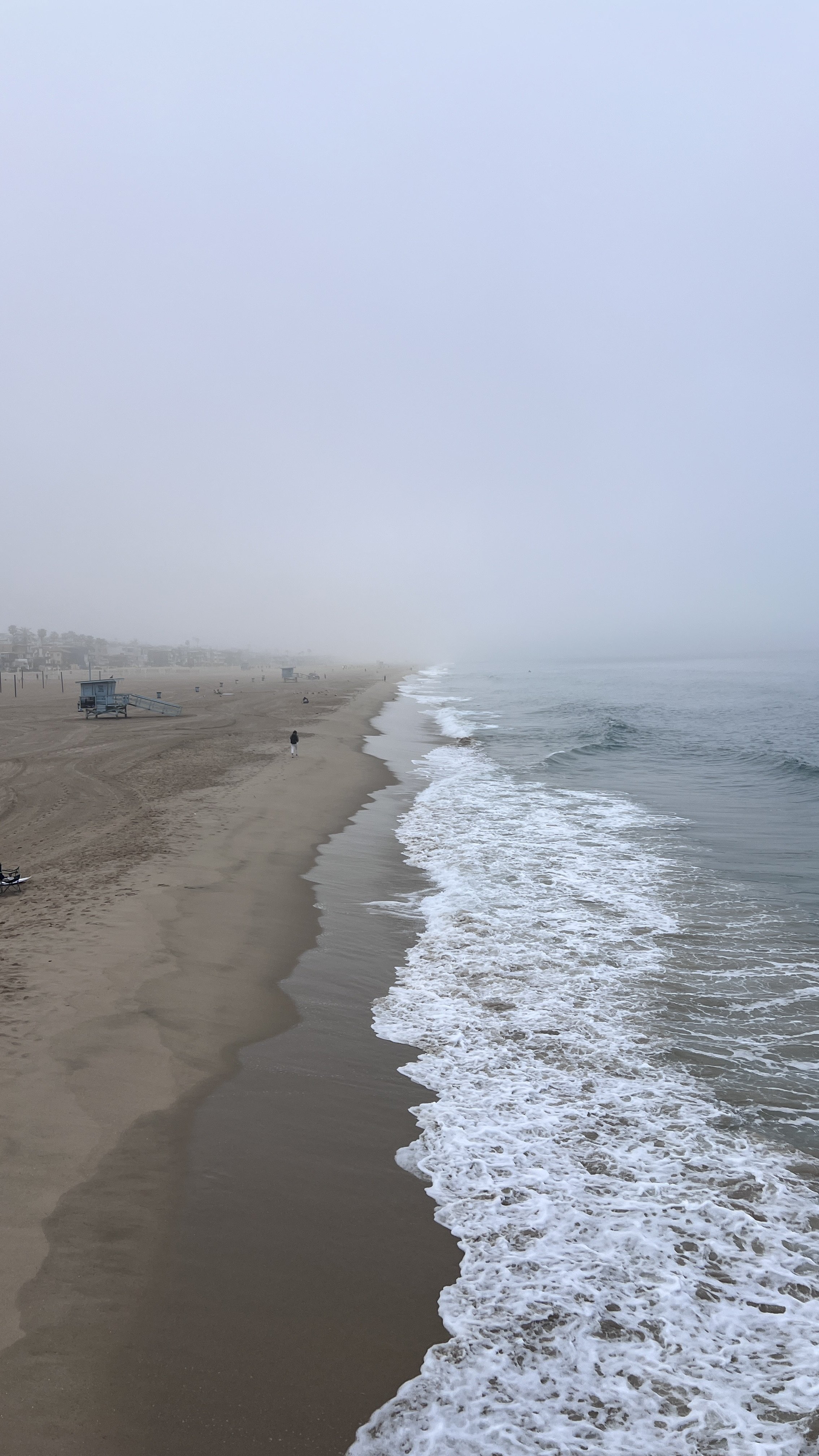 Overcast day at a beach with sandy shore, lifeguard stations, and a few people walking.