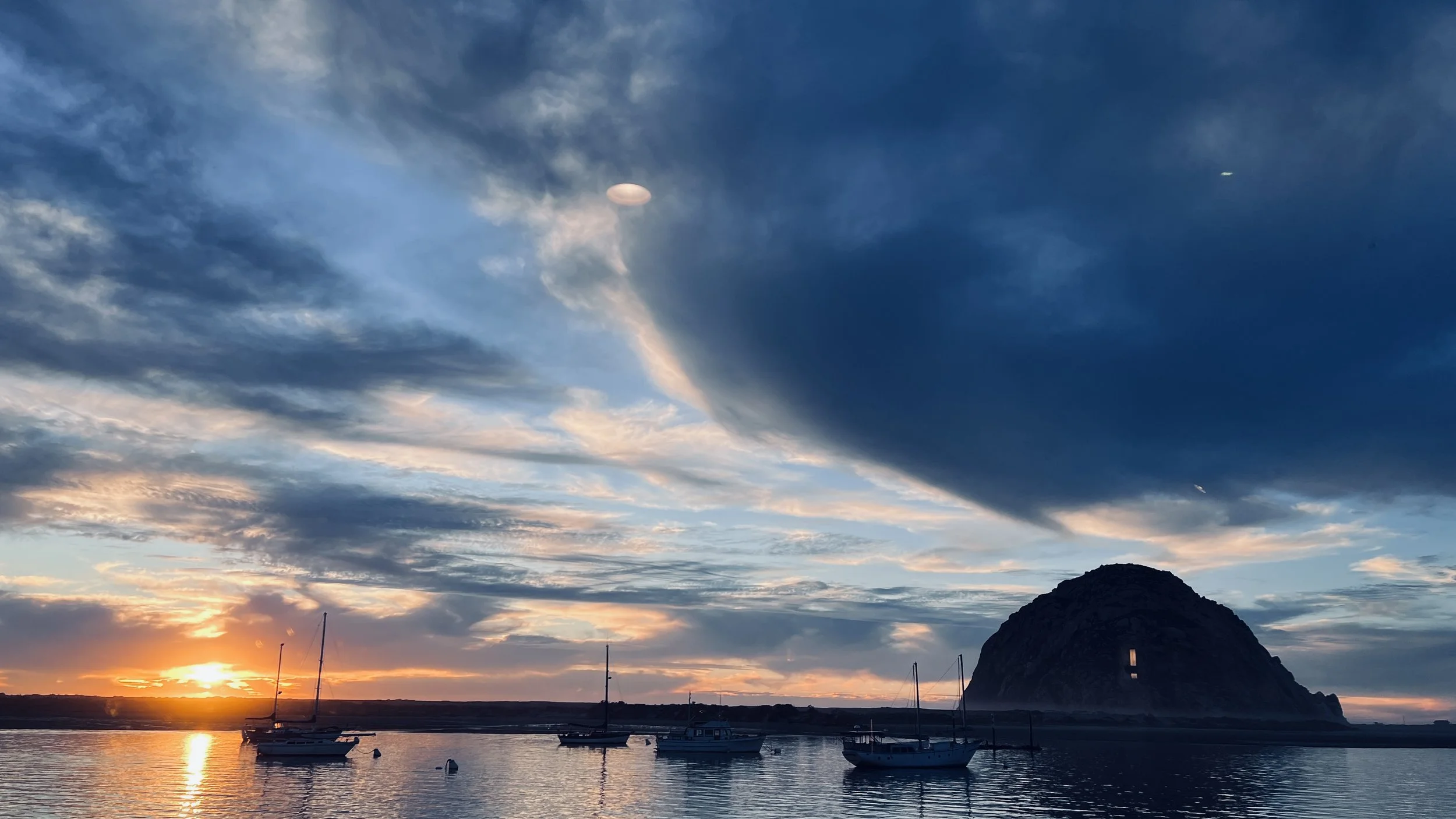 Sunset over a harbor with sailboats and a large mountain in the background.