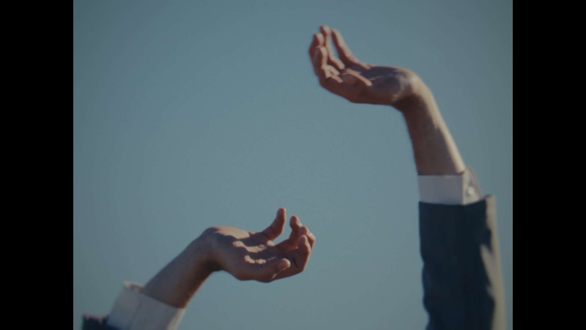 Two hands reaching towards each other against a blue sky, one hand appears to be a mannequin or robotic hand, and the other is a human hand.