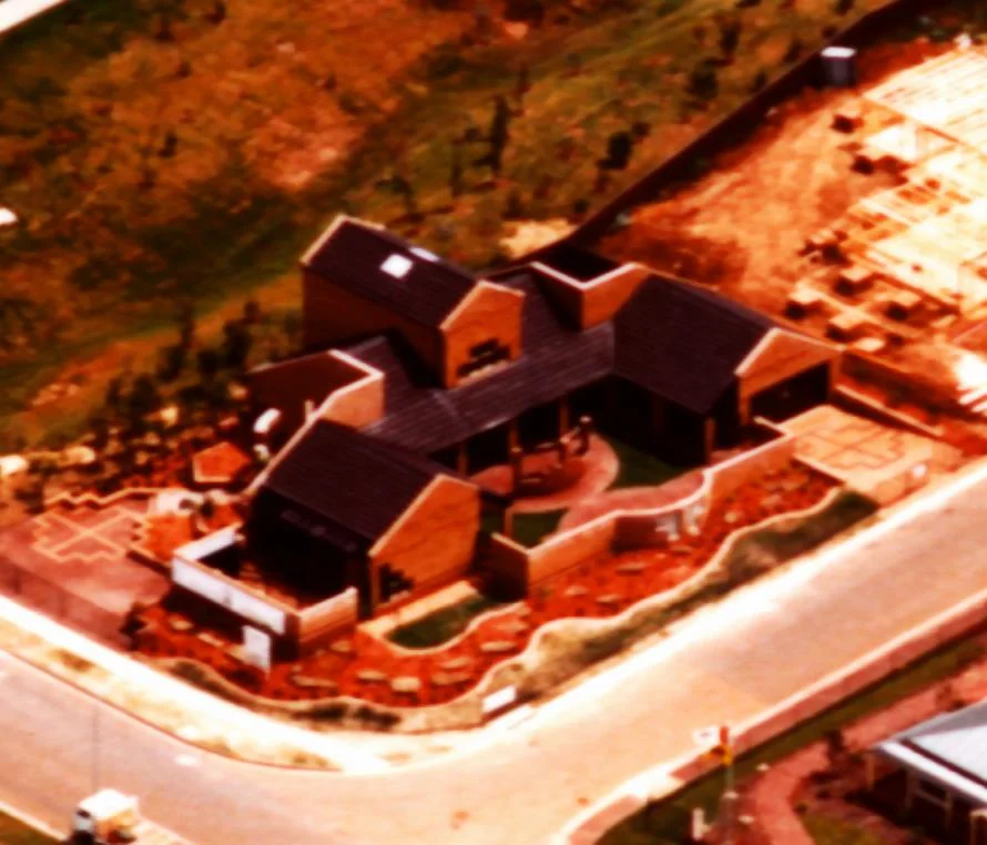 Aerial view of the finished house on its corner site, with dark roofs, brick walls and landscaped courtyards