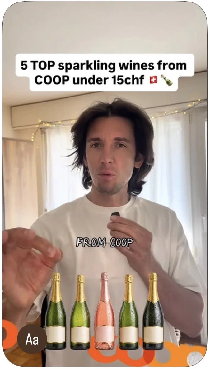A man with long brown hair holding a champagne bottle, standing in front of a table with five bottles of sparkling wine from Coop, some with gold foil and one with pink foil. The text overlay reads "5 TOP sparkling wines from COOP under 15chf." The background features cream-colored curtains and string lights.