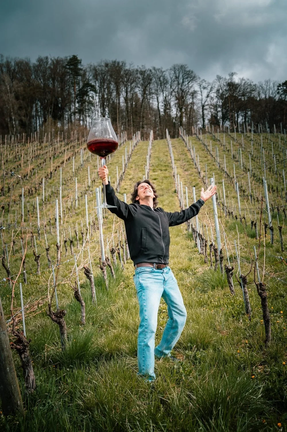 Davide Dellago celebrating in a Swiss vineyard holding a giant glass of red wine