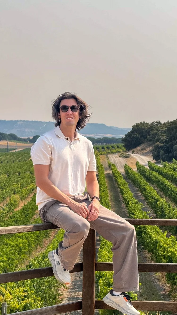 Davide Dellago sitting on a wooden fence above rows of vines