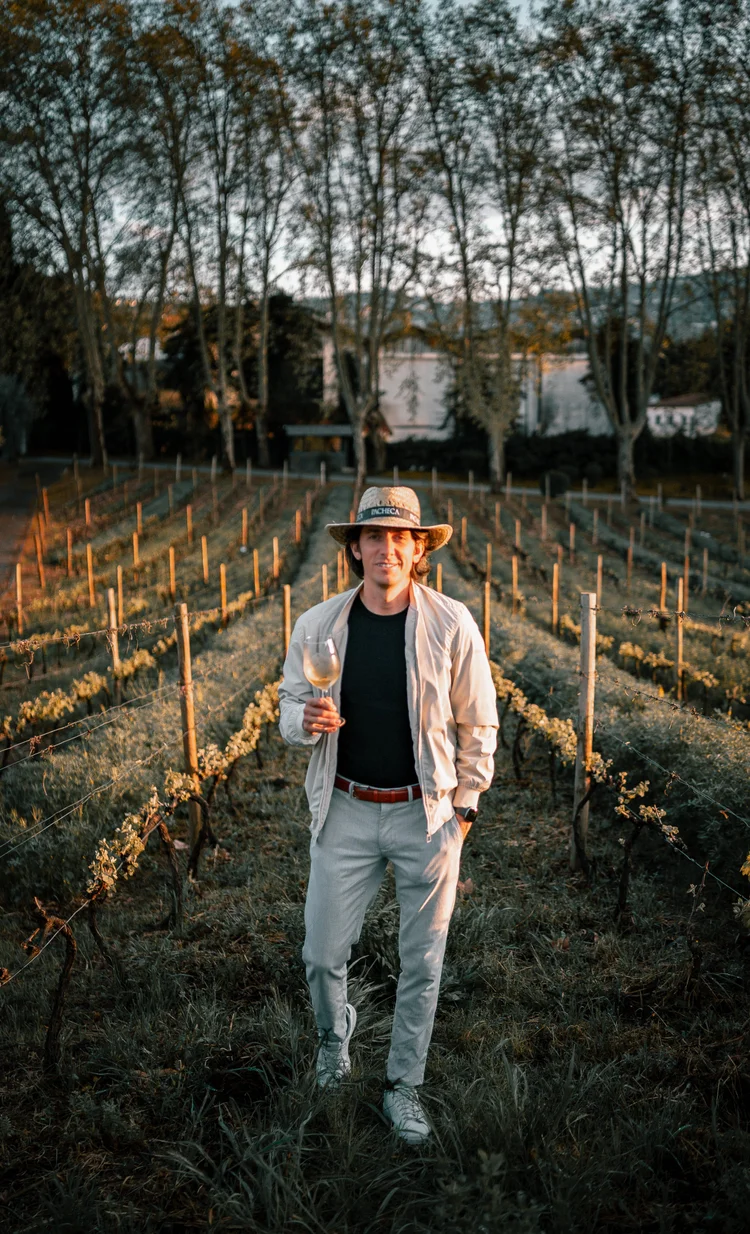 Davide Dellago in a vineyard at golden hour holding a glass of white wine