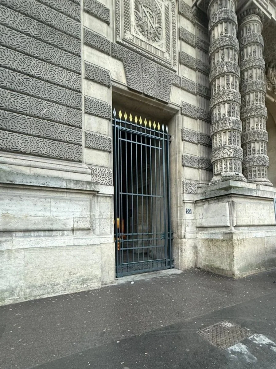 Façade d'un bâtiment en pierre avec des détails architecturaux ornementaux et une grille noire fer forgé sur une porte ou une fenêtre, avec une plaque portant le numéro 93.