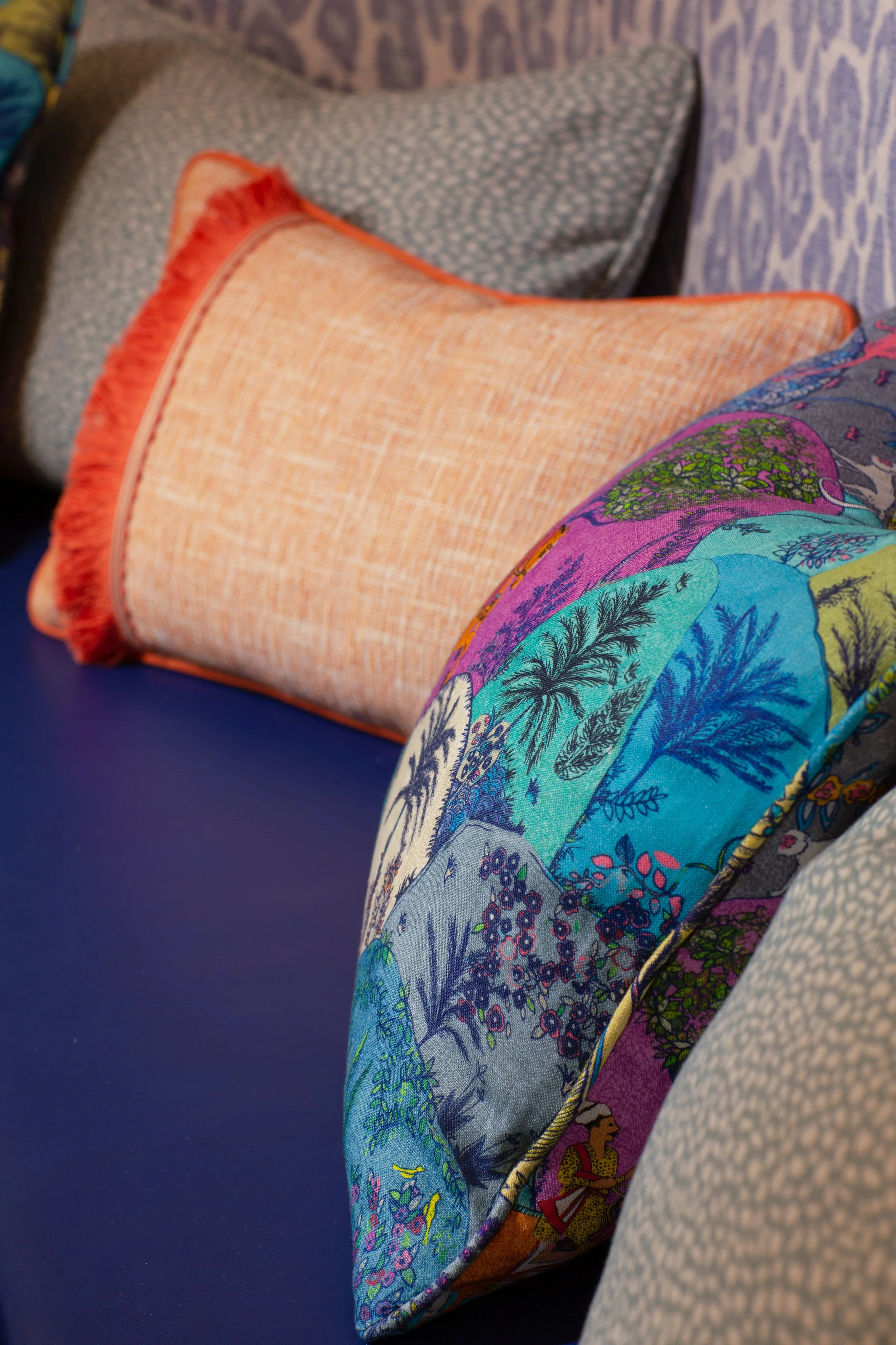 Close-up of colorful embroidered fabric with illustrations of trees, animals, and nature scenes, placed on a surface with patterned and textured textiles in the background.